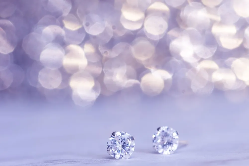 How to clean diamond earrings: sparkling diamond studs on a lilac background