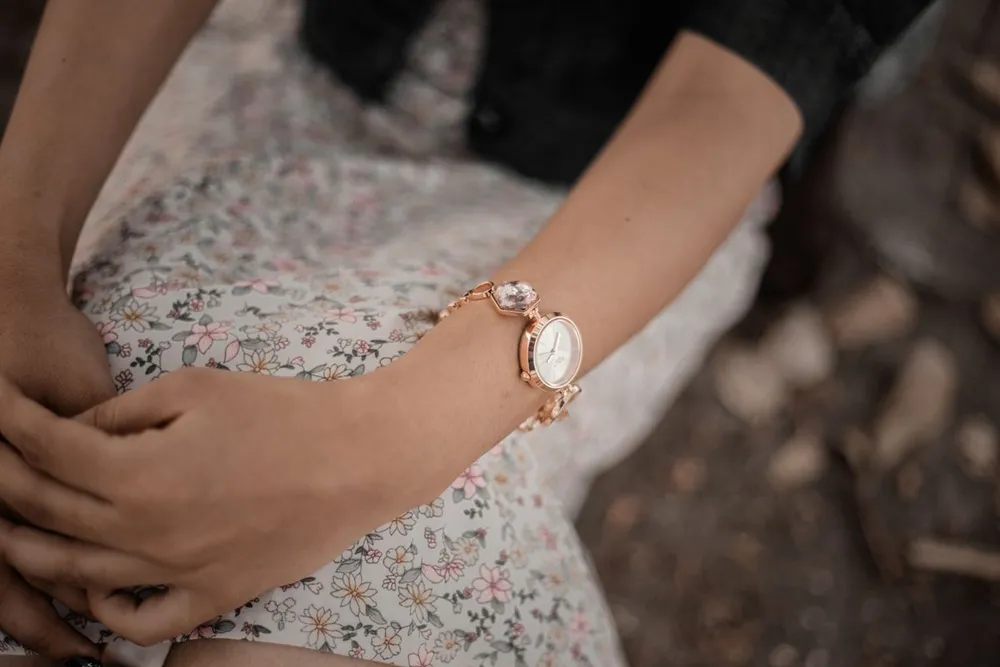 Cartier Baignoire watch guide: a small ladies gold watch on a slim wrist with a floral dress