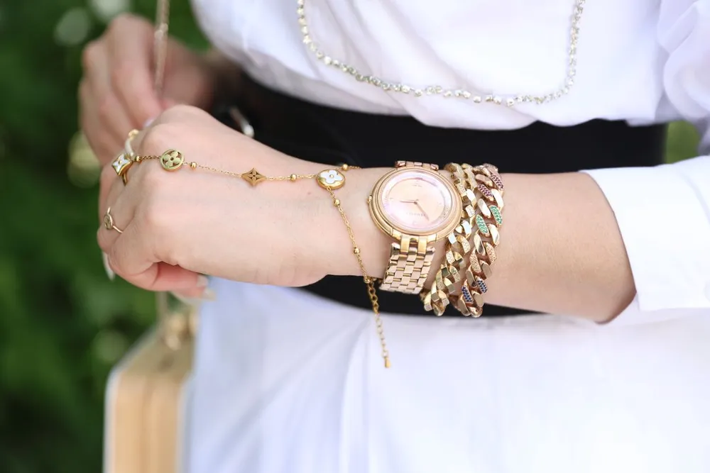 Gold watch stacked with chain bracelets on a wrist, showing how a small watch sits when worn