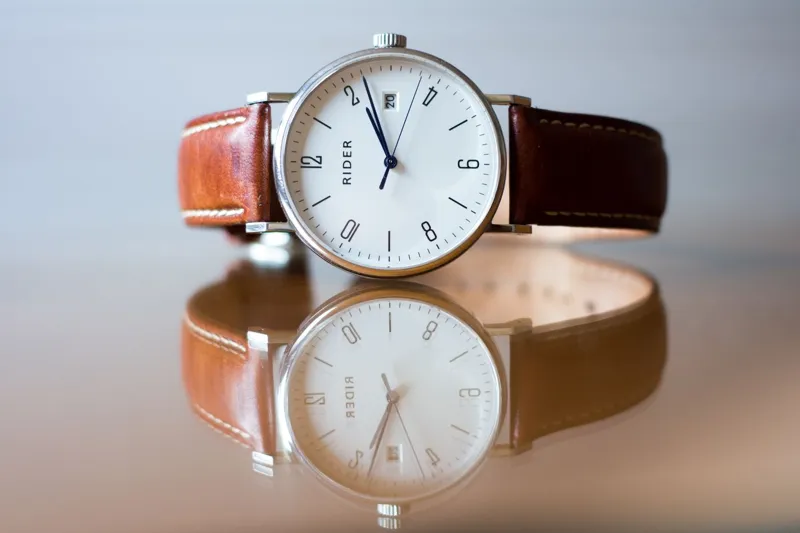 Cartier Tank watch style: a slim wristwatch with a leather strap resting on a reflective surface